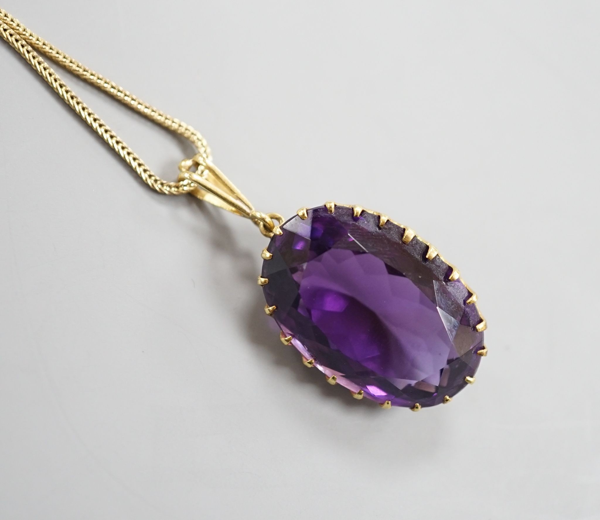 An early 20th century yellow metal mounted oval cut amethyst pendant, overall 37mm, on a yellow metal fine link chain, 49cm, gross weight 10.3 grams.